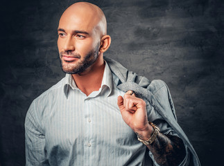 Portrait of a shaved head male with tattooed arm holds jacket on his shoulder.