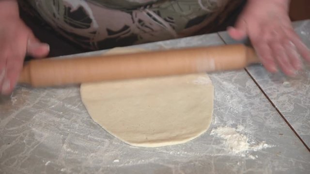 Female hands roll out yeast dough for pizza or bread using a rolling pin on a light table, close-up shot.