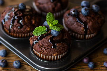 Chocolate muffins with chocolate syrup, blueberries and mint in a wooden background