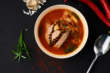 Korean cuisine. Spicy kimchi soup served in a bowl standing on black background.