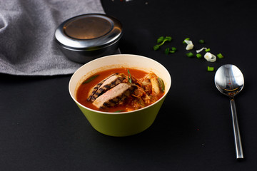 Korean cuisine. Spicy kimchi soup served in a bowl standing on black background.