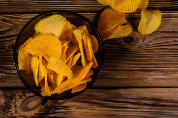 Potato chips in glass bowl on wooden table. Top view