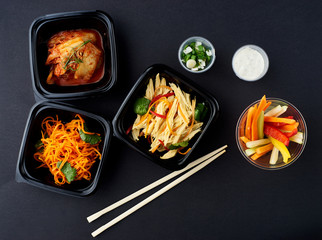 Korean cuisine. Set of salads on black background. Asparagus, korean carrot, kaktugi, fresh vegetable sticks and green onion.