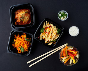 Korean cuisine. Set of salads on black background. Asparagus, korean carrot, kaktugi, fresh vegetable sticks and green onion.