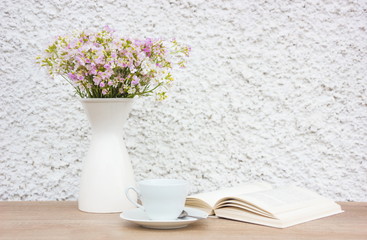 Book, white cup and vase with flowers on wooden table