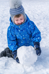 The boy rolls a snowball. A snowball for a snowman.