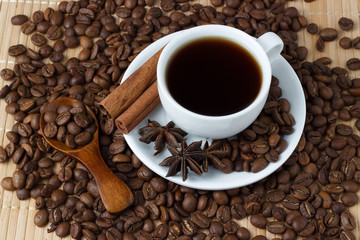 White cup of coffee with anise, cinnamon sticks and a spoon