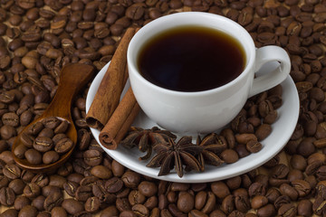 Coffee in a cup with cinnamon sticks and anise on the background of coffee beans