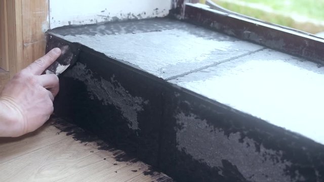 Time lapse with hands of tile worker filling gaps between tiles with a grout using soft rubber spattle in threshold