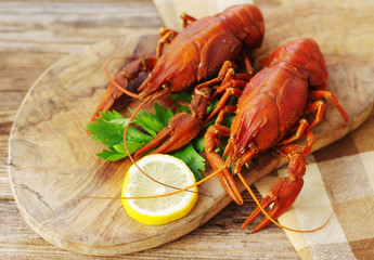 Boiled crayfish with greens and a lemon on a wooden board, close up