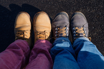 A couple of friends are sitting next to each other. Multicolored pants and shoes. Top-down view