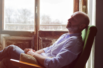 A middle-aged man is tiredly sitting in a chair. He dreams or makes plans