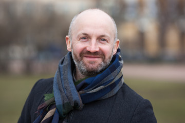 A middle-aged man in a scarf and jacket for a walk around the city.