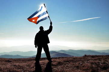 Successful silhouette man winner waving Cuban flag on top of the mountain peak