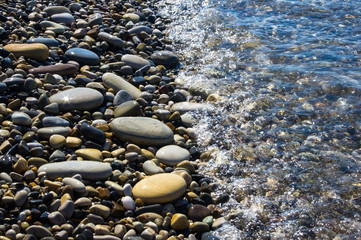 sea pebble beach with multicoloured stones, waves with foam
