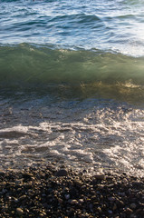 sea pebble beach with multicoloured stones, waves with foam