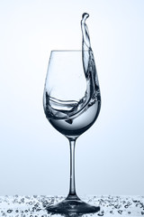 Water splashing from wineglass with drinking cleaner water while standing on the glass against light background.