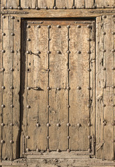 ancient brown wooden door with metallic ornaments on a wooden wall