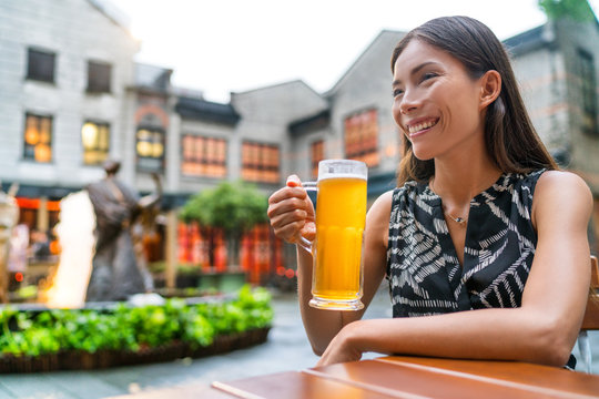 City lifestyle people. Young urban Asian woman drinking a beer pint at outdoor pub on outside terrace in summer. Shanghai modern life on famous Xintiandi shopping and entertainment street.