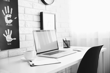 Fototapeta premium Modern home office workspace with laptop, coffee, and family handprints on white brick wall