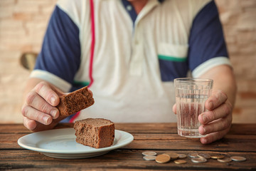 Senior man sitting at table with bread, glass of water and coins, closeup. Poverty concept