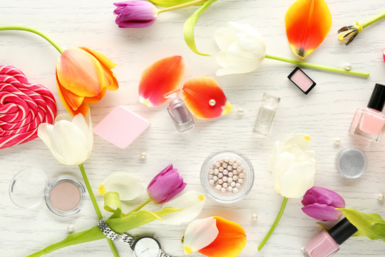 Composition of flowers, cosmetics and accessories on white wooden table
