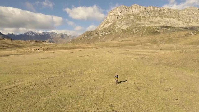 Aerial shot of mountain biker riding the trail on alpine pass in autumn season
