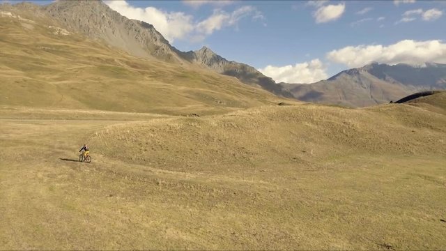 Aerial shot of mountain biker riding the trail on alpine pass in autumn season
