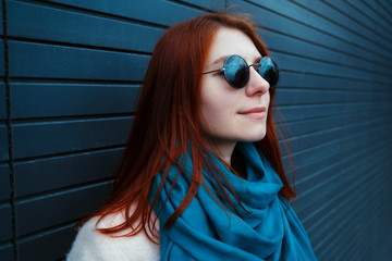 Hipster redhaired girl in stylish sunglasses is posing in front of a black wall on the street