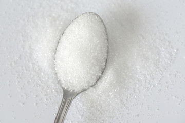 Fototapeta na wymiar Spoon with white granulated sugar on white texture background. Unhealthy food concept.
