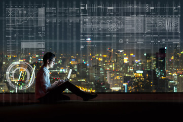 Asian businessman sitting and using the laptop showing digital virtual screen over the cityscape...