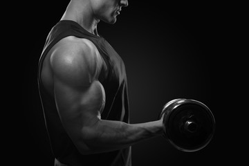 Fototapeta na wymiar Close-up photo of handsome power athletic man in training pumping up muscles with dumbbell. Strong bodybuilder with perfect deltoid muscles, shoulders, biceps, triceps and chest