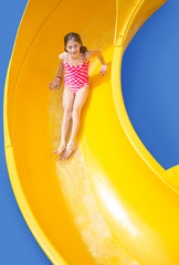 Smiling Young girl riding down a yellow water slide