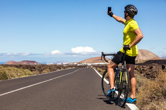 Cyclist tourist taking selfie picture with smartphone during biking trip alone on summer vacation travel. Man riding road bike using phone to take photos during holidays.