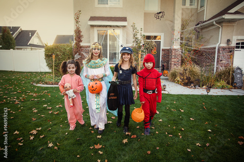 Group of kids dressed in Halloween costumes going trick or treating outdoors in October in a decorated neighborhood