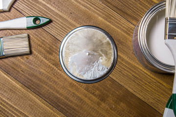 A set of white paint brushes, a metal can with white paint on a wooden texture table