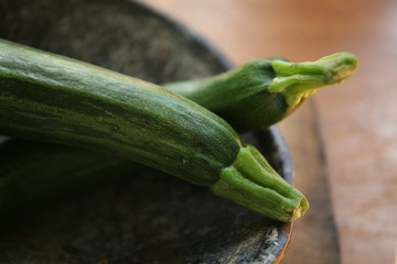 still life with green zucchines in the rustic bowl on the terracotta  background in the daylight in close-up