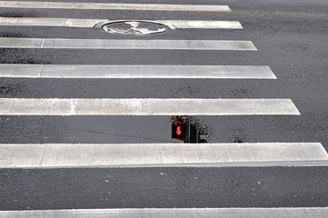 Puddles on a pedestrian crossing seen semaphore signal reflection.
