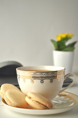  Cup of tea and vanilla French macaroons with yellow plant, laptop computer and a mouse, home office of a freelancer
