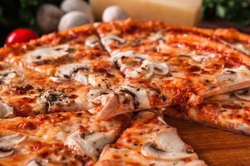 Delicious hot pizza sliced and served on wooden platter with cut slice, close up view. Italian fast food.