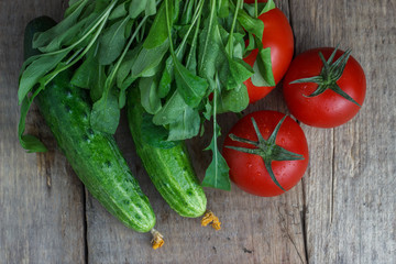 Tomatoes and cucumbers with greens on an old wooden background