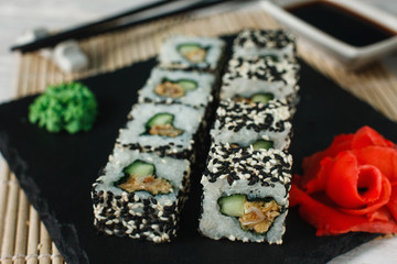 Appetizing and fresh set of uramaki rolls with sesame served on black slate, closeup. Japanese healthy food, sushi, seafood.
