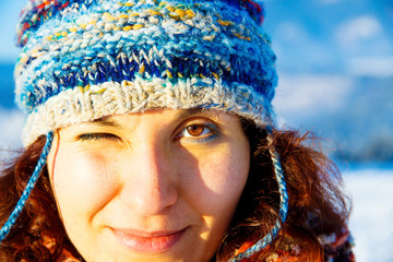 young woman in colorful winter cap blinking with one eye.