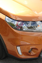Scheinwerfer eines orangen SUV`s im Hochformat
