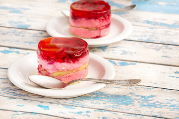 Two cakes on saucers with tea spoons on old blue wooden background.