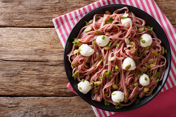 Beetroot pasta with mozzarella cheese, pumpkin seeds and greens close-up. Horizontal top view