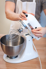 A man is beating an egg cream, a creamer with a mixer, close-up of a hand include a mixer