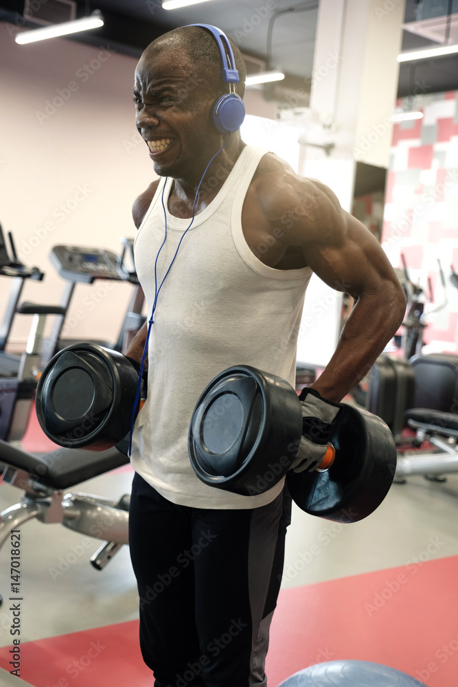 Wall mural muscular black man doing exercises with dumbbells at gym