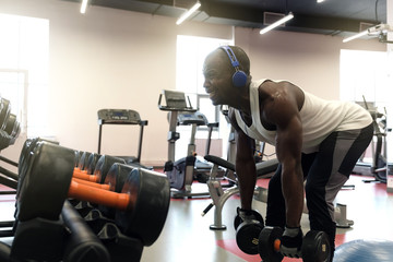Fototapeta na wymiar Muscular black man doing exercises with dumbbells at gym