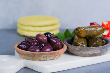 Mediterranean appetizer antipasti tapas bowls with green and calamata olives, feta cheese, stuffed pepper with garlic pita bread, herbs on white marble plank